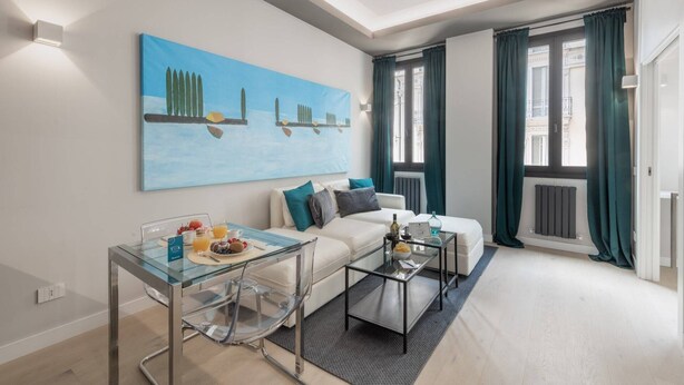 A modern living room with a glass coffee table, a white sofa, and a painting on the wall. - Sweett | Duomo V - One Bedroom Apartment, Sleeps 3 (Milano)