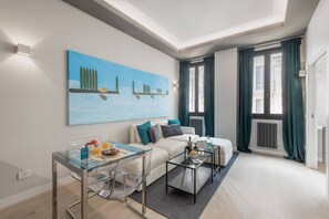 Een moderne woonkamer met een glazen salontafel, een witte bank en een schilderij aan de muur.