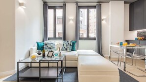 A modern living room with a sofa, a glass coffee table, and a dining area with a glass table and chairs.