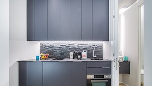 A modern kitchen with dark cabinets, a stone backsplash, a kettle, a coffee maker, and an oven.