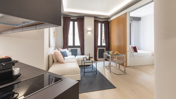 A modern apartment with a kitchen, a living area with a sofa, a dining table, and a small balcony.