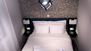 A hotel room with a stone wall, a bed with white linens, two bedside lamps, and two folded towels on the bed. - Athens Chic House Apt A3 40sq.m (Athina)