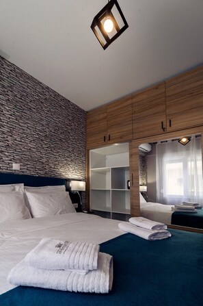 Ein modernes Hotelzimmer mit Wand im Steinoptik, einem großen Bett mit weißer Bettwäsche, einem Holzschrank und einem eingebauten Spiegel.
