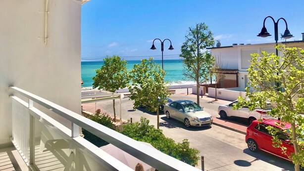 Un balcón con vista al mar, un estacionamiento con coches y un edificio con el número 12.