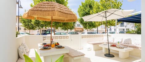 An outdoor patio with a table set for breakfast, a thatched umbrella, and a seating area with cushions.