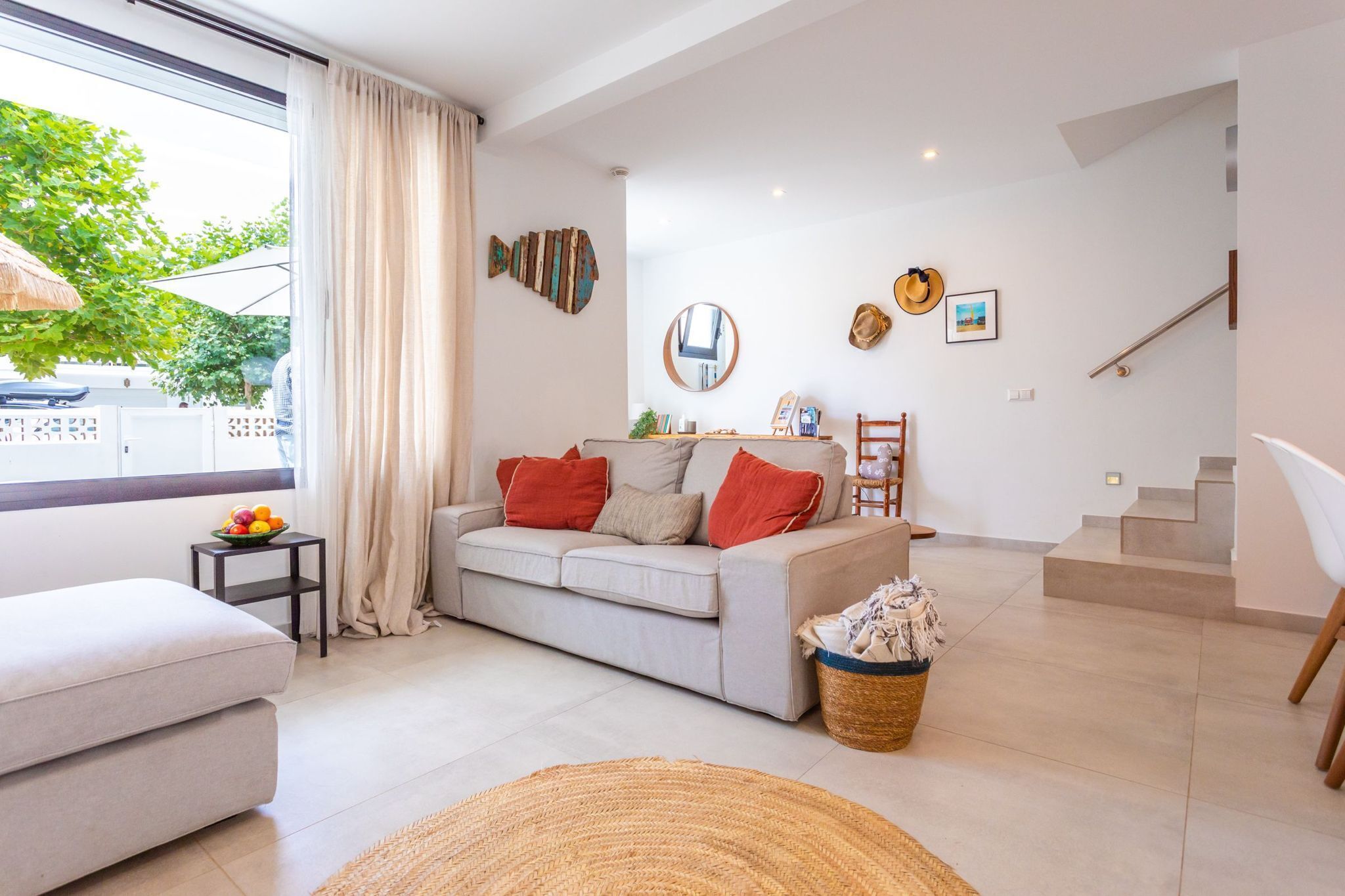 Una sala de estar moderna con un sofá, una pequeña mesa con fruta, una cesta de mimbre y una escalera.