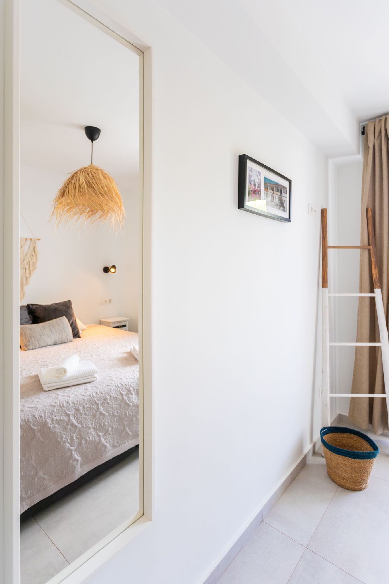 Un dormitorio con una cama, un lámpara colgante, un cuadro enmarcado en la pared, una escalera y una cesta tejida en el suelo.