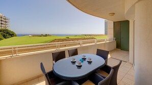 A balcony with a table and chairs, a view of a golf course, and a building in the background. - SEAFRONT LUX APART inc POOL, Upmarket Area (Sliema)
