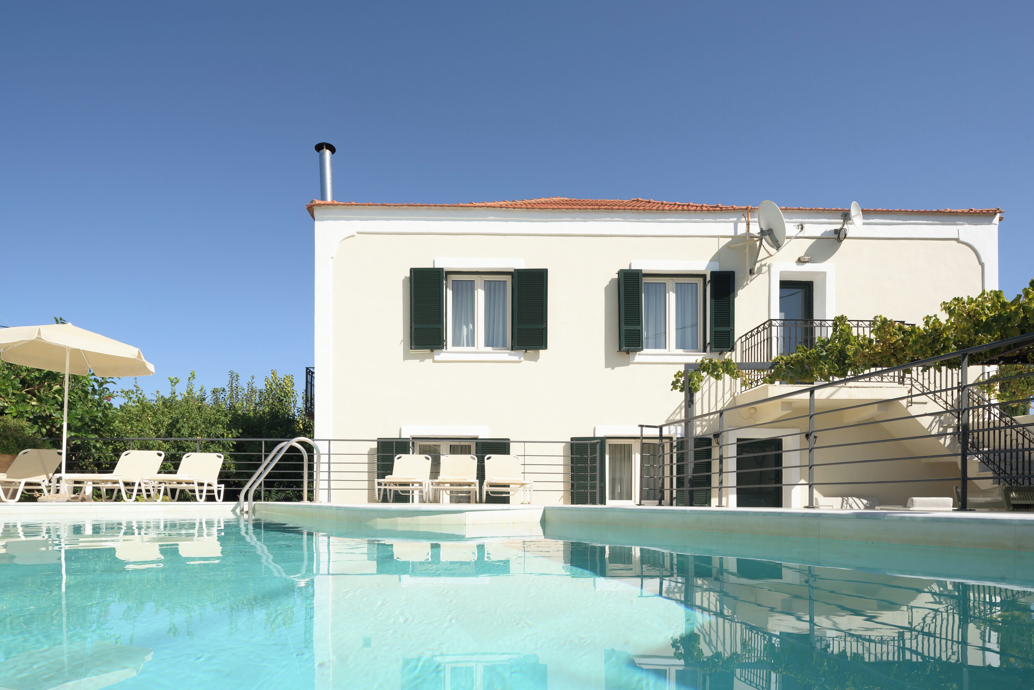 A pool area with lounge chairs and a building with a tiled roof.