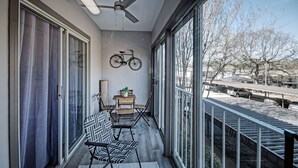 Un balcón con ventilador de techo, una bicicleta montada en la pared, una mesita con una planta y un rincón de descanso con sillas y un banco.