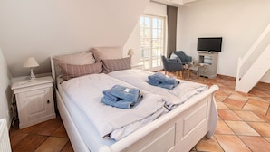 Une chambre à coucher avec un lit, une table de chevet, une chaise, un téléviseur et une fenêtre.