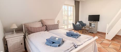 Quarto com cama, mesa de cabeceira, cadeira, televisão e janela.