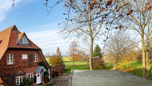 Une maison en briques rouges, avec un toit en pente, un petit garage attenant et une allée pavée.