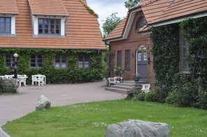A courtyard with a brick building, white chairs, and a stone bench. - Das Backhaus 3 (Stoltebuell)