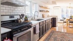 A modern kitchen with a stainless steel stove, white tiled backsplash, and wooden flooring. - Rondout Retreat: Private Poolside Luxury with Hot Tub, Sauna and Fire Pit (Rosendale)