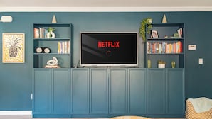 A living room with a TV displaying 'NETFLIX' on the screen, surrounded by bookshelves and a coffee table with a remote control. - Rondout Retreat: Private Poolside Luxury with Hot Tub, Sauna and Fire Pit (Rosendale)