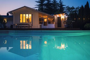 Une maison avec une piscine, un patio couvert et un petit bâtiment attenant doté d’une porte et de fenêtres.