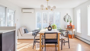A bright, spacious dining area with a wooden table and chairs, large windows, and a modern chandelier. - Rondout Retreat: Private Poolside Luxury with Hot Tub, Sauna and Fire Pit (Rosendale)