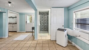 A laundry room with a dryer, a door leading to a tiled shower area, and a kitchen with cabinets and a countertop.