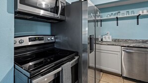 A kitchen with stainless steel appliances, a microwave, oven, refrigerator, and a dish rack.