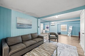 A living room with a sofa, a chair, a coffee table, and a painting on the wall.
