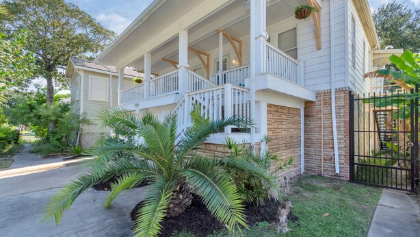 A two-story house with a covered porch, brick foundation, and a black metal gate.