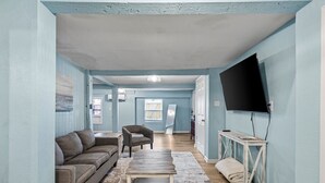 A room with a sofa, armchair, wooden coffee table, and a TV mounted on the wall.