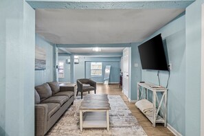 A room with a sofa, armchair, wooden coffee table, and a TV mounted on the wall.