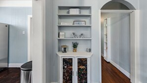 A hallway with a white console table, shelves with decorative items, a framed fish picture, and a stained glass cabinet.