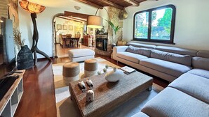 A cozy living room with a wooden ceiling, a fireplace, a large window, and a dining area in the background. - Private Boutique Villa in Rome – Pool, Jacuzzi & Garden, 20min to City (Rome)