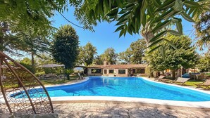 A swimming pool with a stone deck, surrounded by lounge chairs and umbrellas, with a building in the background. - Private Boutique Villa in Rome – Pool, Jacuzzi & Garden, 20min to City (Rome)