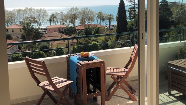 A balcony with a table and chairs, a view of the sea, and a row of houses in the background. - Neptune 5, top floor (Menton)