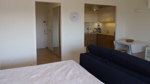 A compact room with a bed, a dark blue sofa, a small table, and a kitchenette area. - Neptune 5, top floor (Menton)