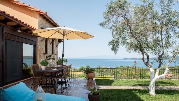 Um pátio com mesa e cadeiras, piscina e vista para o mar.