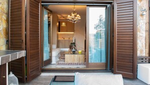 Interior moderno com porta de vidro deslizante que dá para uma cozinha e sala de estar, com um candelabro, um sofá e uma mesa de centro.
