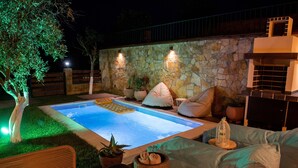 Piscina com parede de pedra, móveis de exterior e plantas em vasos.