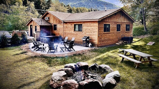 Une cabane en bois dotée d’un patio, de meubles de jardin et d’un foyer extérieur.
