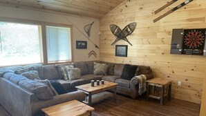 Un salon chaleureux avec un plafond en bois, un canapé d’angle, une table basse et un jeu de fléchettes.