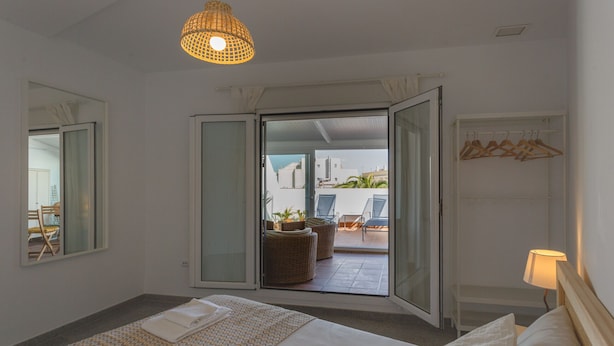 Et hotelværelse med en seng, en hængende lampe, en skydedør til en balkon og et garderobeskab med bøjler.