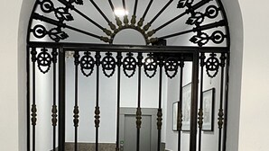 En sort jernport med indviklede detaljer, et nøglehul og et skilt med teksten "NO Portas, por favor, cierre, cuidado, gracias".