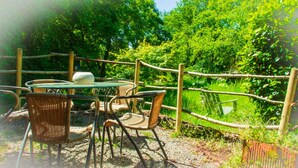 Un espace extérieur aménagé avec des chaises en osier et une table en verre, entouré d’une clôture en bois et d’une végétation luxuriante.