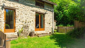 Une maison en pierre avec deux fenêtres, une terrasse en bois et une clôture en bois.