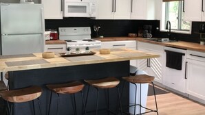 Een moderne keuken met witte kasten, een centraal eiland met krukken, hanglampen en een roestvrijstalen koelkast.