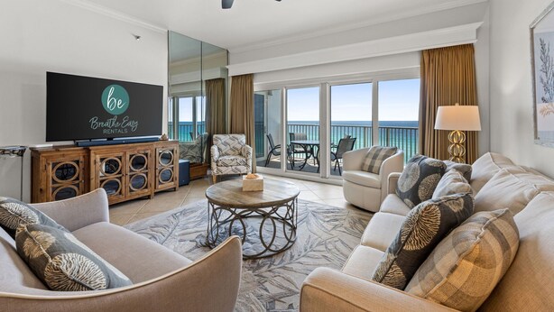 A spacious living room with a large flat-screen TV, comfortable seating, a ceiling fan, and a view of the ocean through large windows. - Beachfront Escape! Perfect Beach! Relax by the Pool! Beach Manor 808 is Waiting! (Miramar Beach)