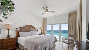 A bedroom with a large bed, wooden headboard, two bedside tables with lamps, a view of the ocean, and a ceiling fan. - Beachfront Escape! Perfect Beach! Relax by the Pool! Beach Manor 808 is Waiting! (Miramar Beach)