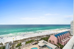 A beach view from a high-rise building with a pool, beach umbrellas, and a clear sky.
