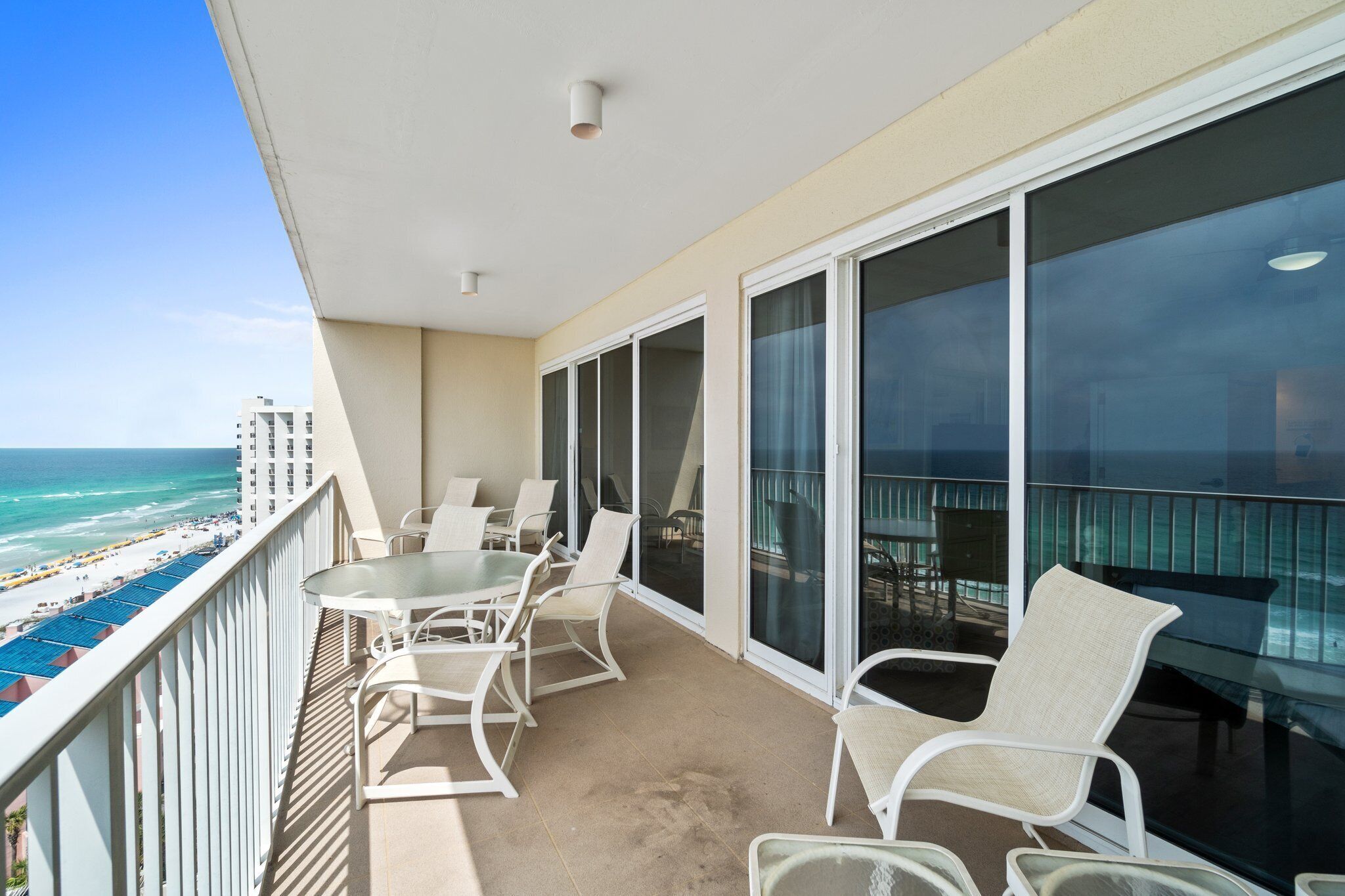 Un balcon avec une porte vitrée, des chaises blanches et une table donnant sur la plage.