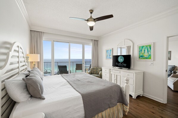 A hotel room with a bed, a television, a desk, and a balcony with a view of the ocean.