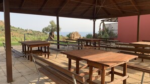 An outdoor covered patio with wooden tables and benches, overlooking a hilly landscape. - 35 sqm apartment with seafront veranda (2) (Sciacca)
