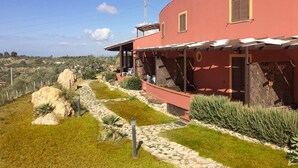 A red building with a covered patio, a stone pathway, and a view of the countryside. - 35 sqm apartment with seafront veranda (2) (Sciacca)